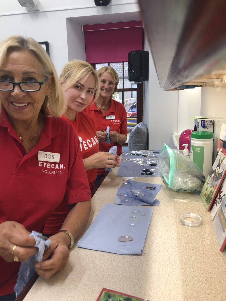 Image shows 3 lady volunteers wearing red EYECAN shirts cleaning spectacle lens