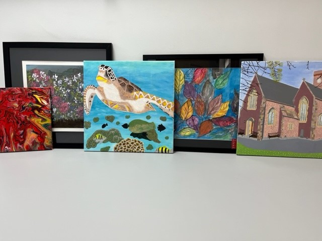 Image shows a collection of brightly coloured art work. The art work is sitting on two shelves with 5 pieces on each shelf